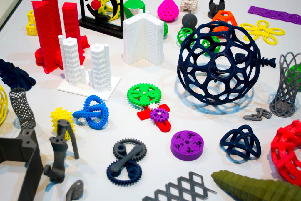 Colorful assortment of 3D-printed prototypes, including geometric shapes, gears, and architectural models