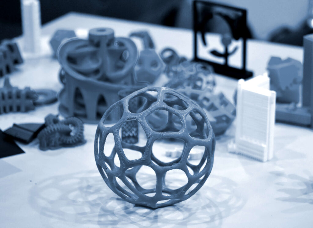 Intricate 3D-printed prototypes, including a geometric sphere and complex structures, on a marble surface
