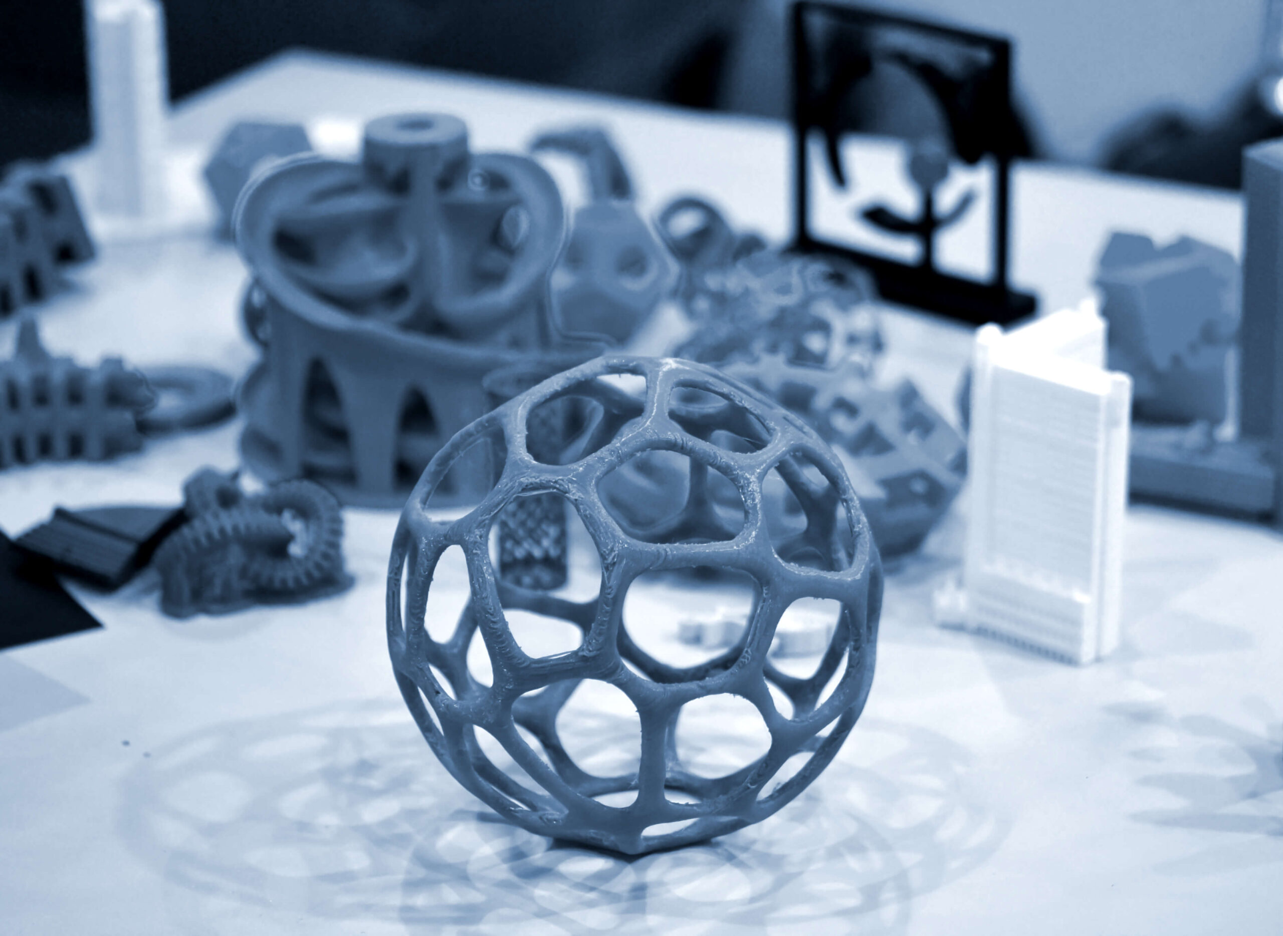 Intricate 3D-printed prototypes, including a geometric sphere and complex structures, on a marble surface