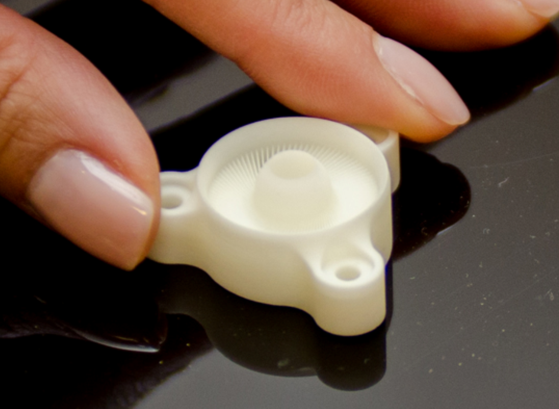 Small 3D-printed white component held between fingers, showcasing intricate details.