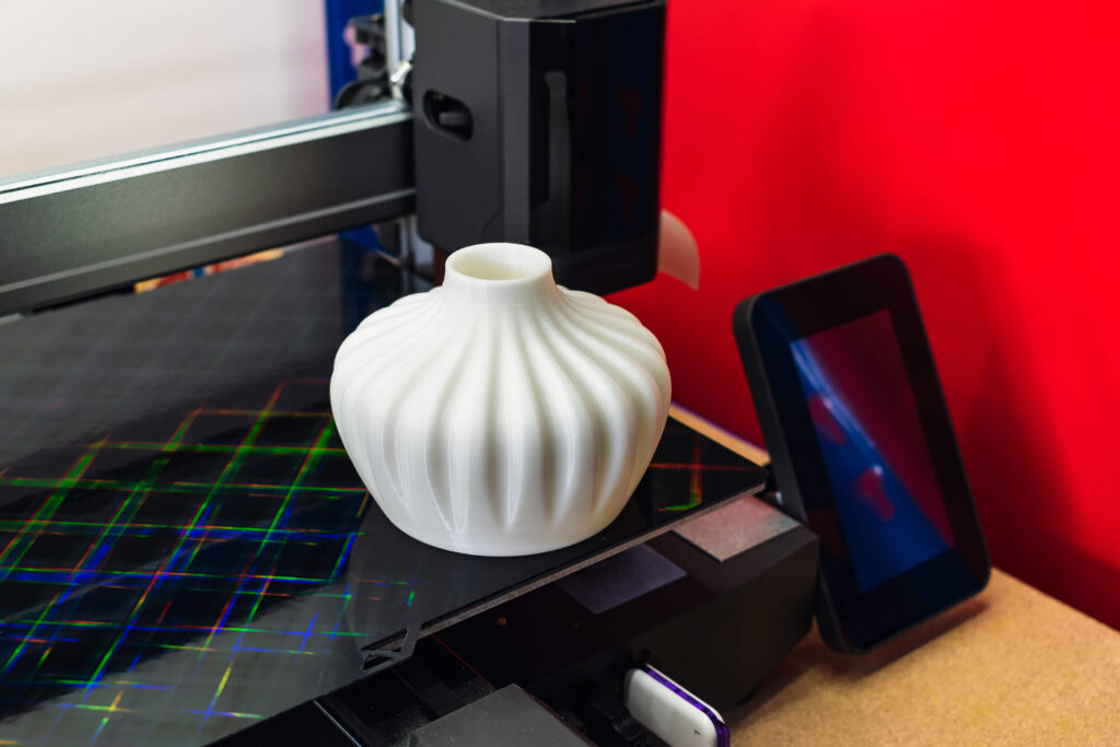White 3D-printed vase with a textured design on a 3D printer bed